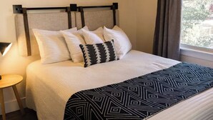 A neatly made bed with a patterned throw, a bedside table with a lamp, and a window with curtains. - Yosemite Cottage Retreat: 1/2 Block to Downtown (Mariposa)
