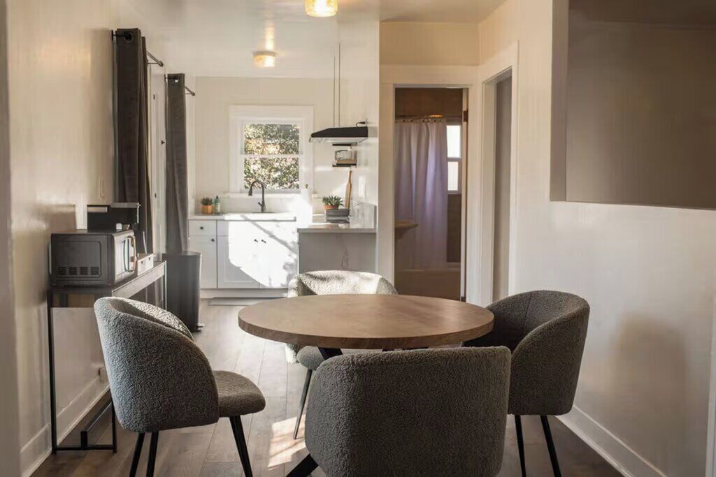Une cuisine moderne avec un coin repas, comprenant une table ronde en bois et quatre chaises grises à revêtement rembourré.