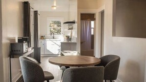 A modern kitchen with a dining area, featuring a round wooden table and four grey upholstered chairs. - Yosemite Cottage Retreat: 1/2 Block to Downtown (Mariposa)