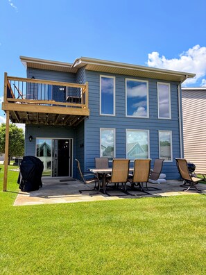 A two-story house with a balcony, a covered patio with a table and chairs, and a lawn. - Family-friendly cabin with ideal proximity to pool (Arnolds Park)