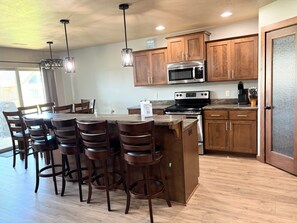 A kitchen with wooden cabinets, a stainless steel microwave, a stove, and a bar area with stools. - Family-friendly cabin with ideal proximity to pool (Arnolds Park)