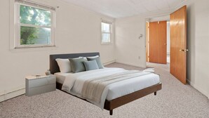A bedroom with a bed, nightstand, and a wooden door. - Fabulous 4-bedroom house with AC in charming Rexhame Beach (Marshfield)