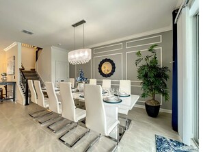 A dining area with a white table set for six, a chandelier, and a potted plant. - Family Reunion Gem! Lakeview, 15min2 parks, pool, spa, theater, Vgames, karaoke (Kissimmee)