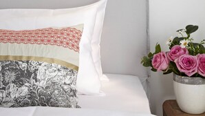 Un lit avec trois oreillers, chacun ayant un motif différent, et un vase rempli de fleurs roses posé sur une table de chevet en bois.