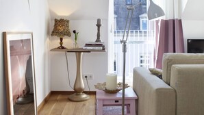 Un salon chaleureux avec un canapé, une petite table sur laquelle se trouve une lampe, un tableau encadré et une fenêtre avec des rideaux.