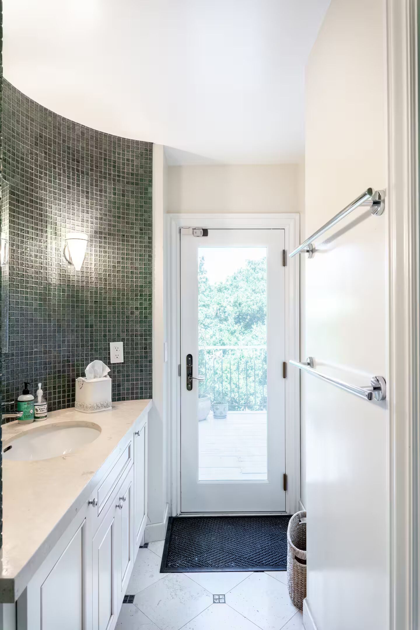 A bathroom with a white sink, a green mosaic wall, and a door leading to a balcony.