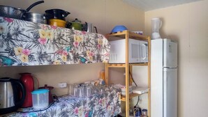 Een keuken met een magnetron, waterkoker en verschillende pannen en kookpotten op planken.