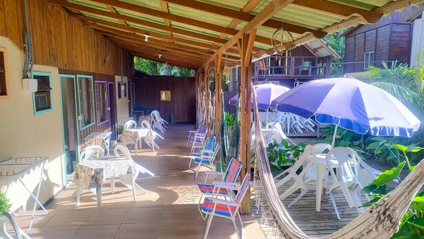 Een overdekt buitengebied met tafels, stoelen, een hangmat en parasols voor schaduw.