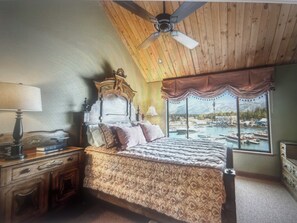 Ein Schlafzimmer mit einem großen Bett, Holzbalkendecke und Blick auf einen Hafen durch ein Fenster.