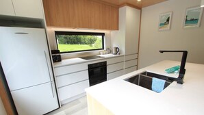 Een moderne keuken met witte kastjes, een inbouwoven, een vaatwasser en een raam met uitzicht op een tuin.