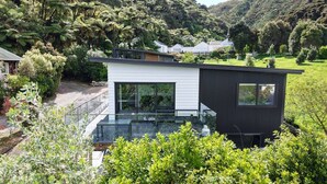 Een modern huis met een glazen balkon, omringd door weelderig groen en heuvels.