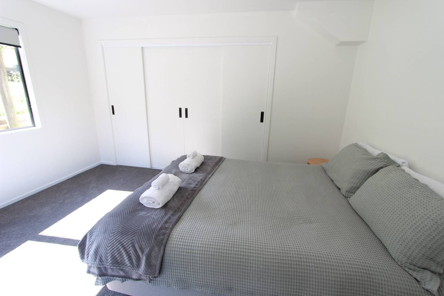 A bedroom with a bed, two towels, a wardrobe, and a window.