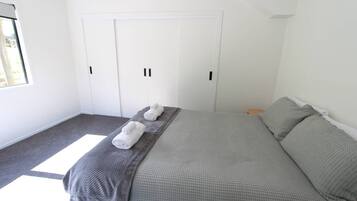 A bedroom with a bed, two towels, a wardrobe, and a window.
