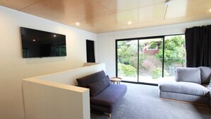 Een moderne woonkamer met een bank, fauteuil en een flatscreen televisie aan de muur.