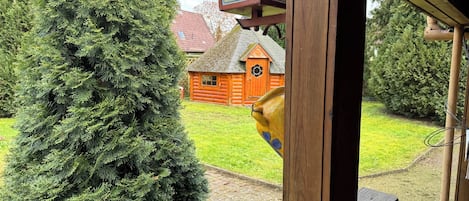 A wooden structure with a large evergreen tree in the foreground and a log cabin in the background.