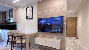 Een moderne woonkamer met een flatscreen televisie aan de muur, een eethoek met twee stoelen, en een houten deur.