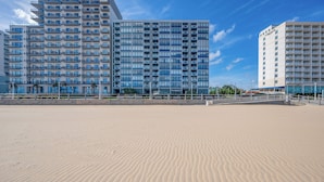 Un hôtel en bord de mer composé de plusieurs immeubles de grande hauteur, avec une plage de sable en premier plan et un ciel bleu dégagé.