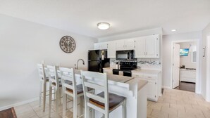 A modern kitchen with white cabinetry, a black refrigerator, a microwave, and a stove. There are four white chairs with wooden seats and a round wall clock. - Beautifully Updated Lakefront Condo – Cozy, Quiet, and Close to the Action! (Osage Beach)