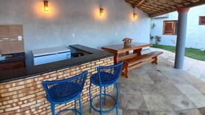 An outdoor kitchen area with a brick counter, two blue chairs, a wooden table, and a pergola overhead.