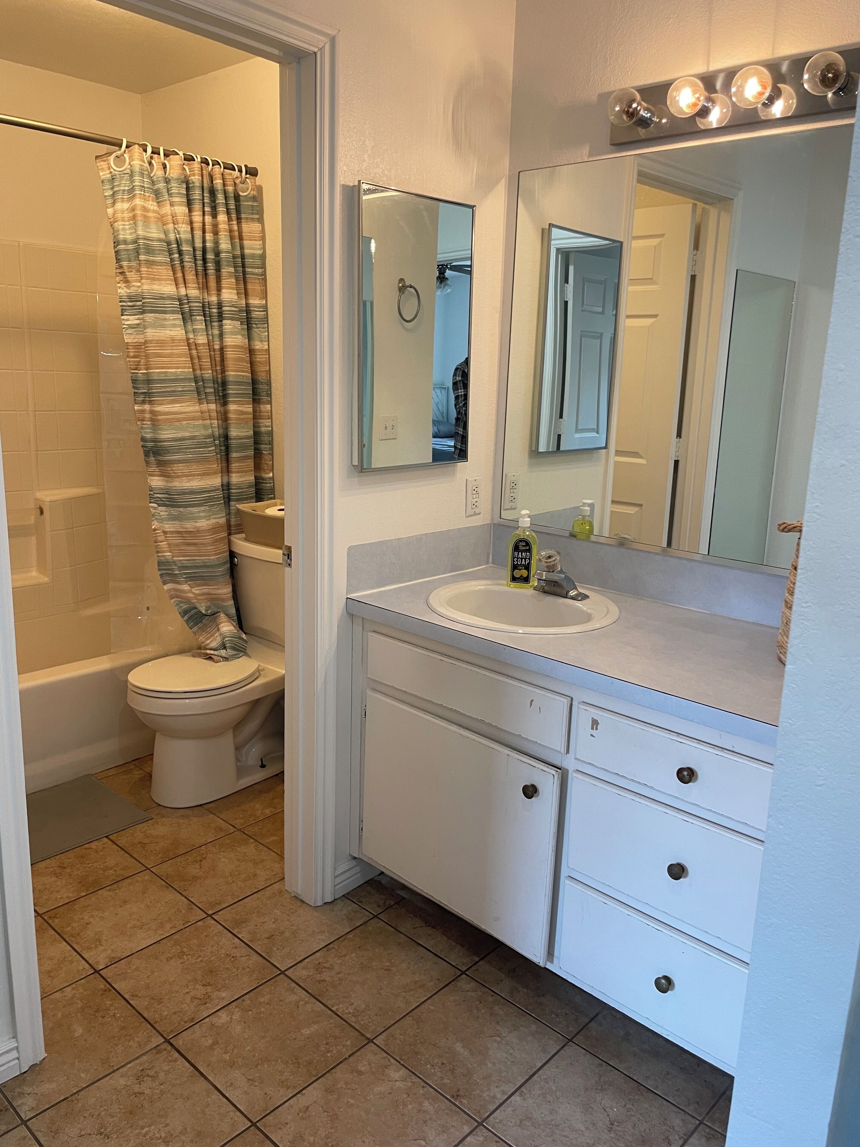 A bathroom with a shower, toilet, sink, and mirror.