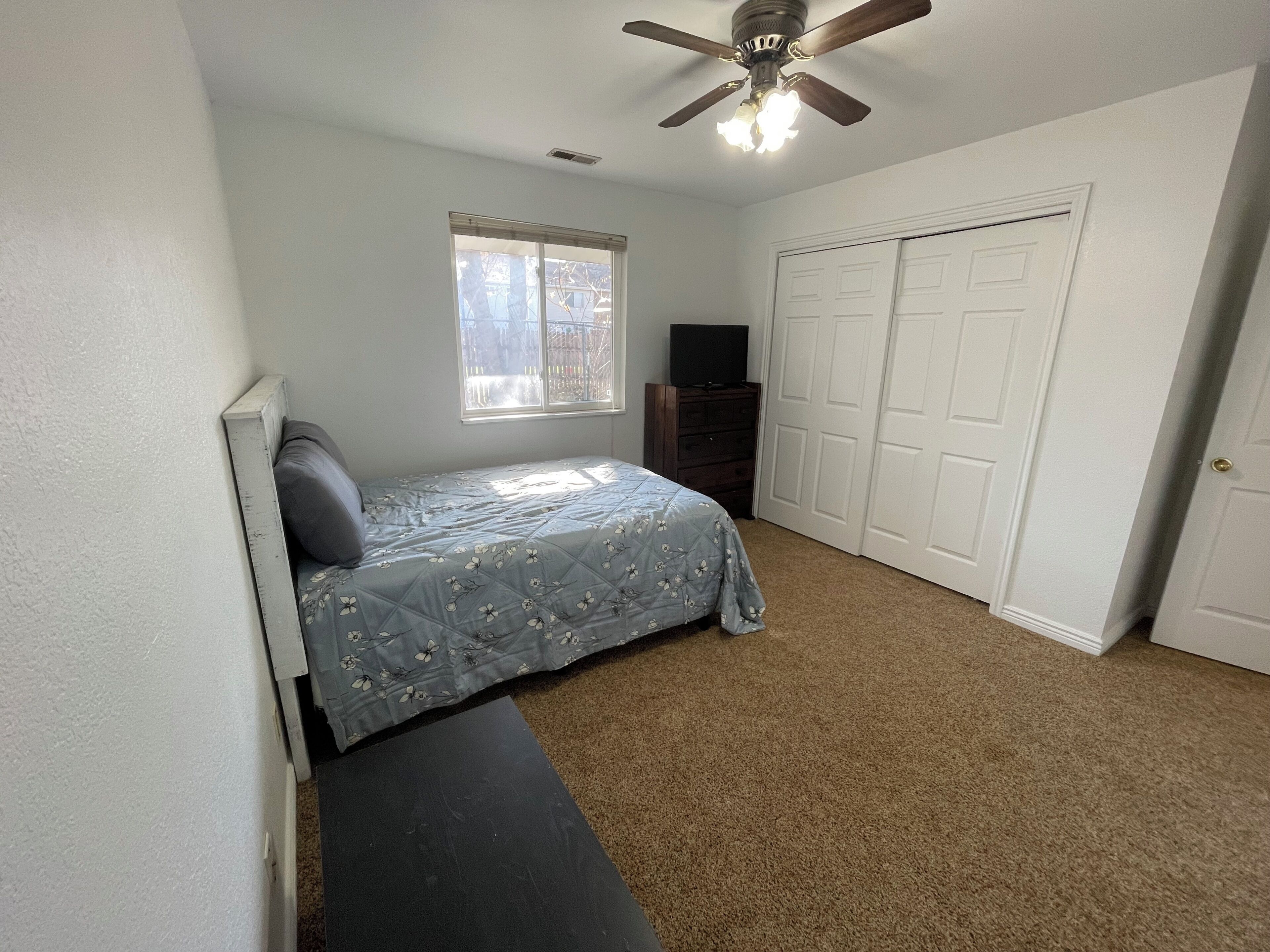 Une chambre à coucher avec un lit, un ventilateur de plafond, une fenêtre, une commode et un placard.