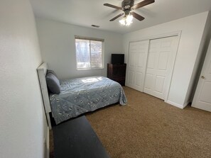A bedroom with a bed, a ceiling fan, a window, a dresser, and a closet.