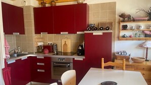 Una cocina compacta con armarios rojos, una encimera blanca y una mesa de comedor.