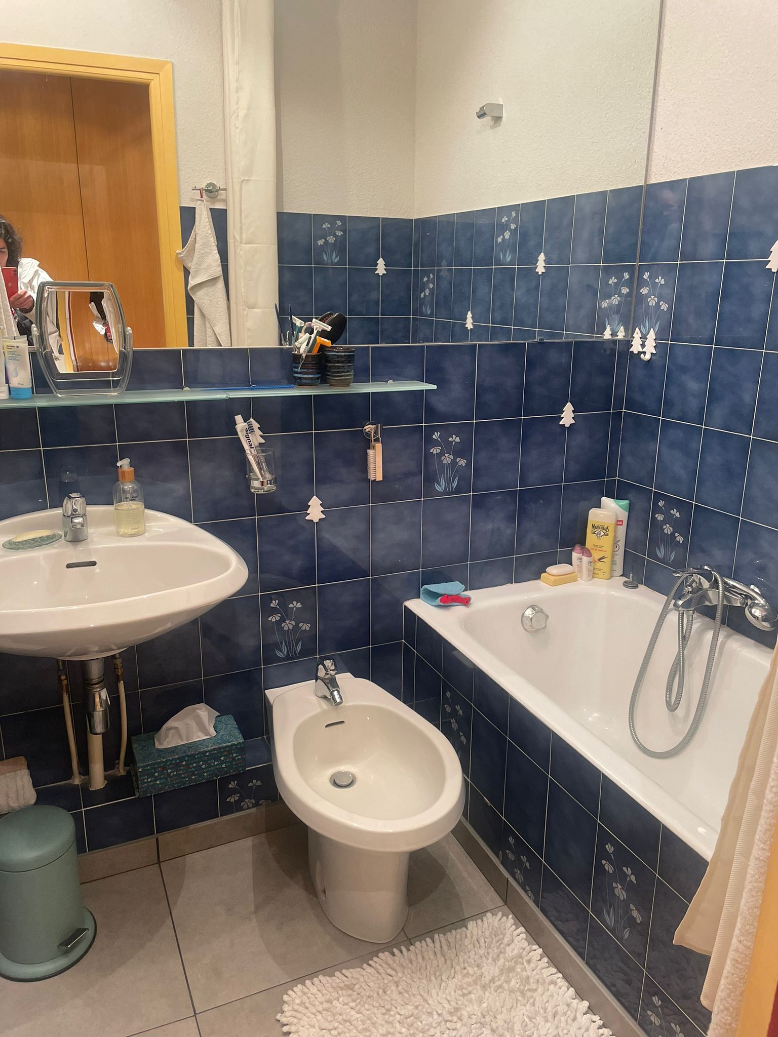 Ein Badezimmer mit Waschbecken, Bidet und Badewanne, mit blauen Fliesen und einem Spiegel.