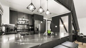 Una cocina moderna con electrodomésticos de acero inoxidable, una isla de mármol y taburetes negros.