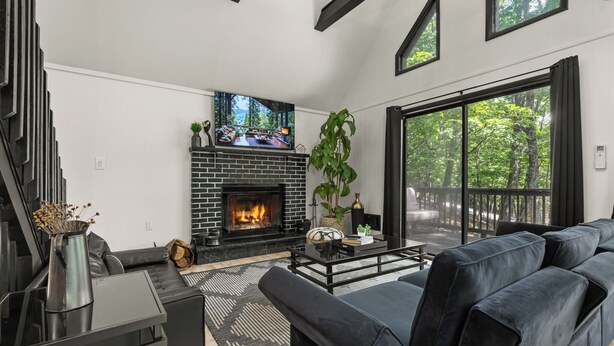 Una sala de estar moderna con chimenea, sofá de cuero negro y ventanas amplias.