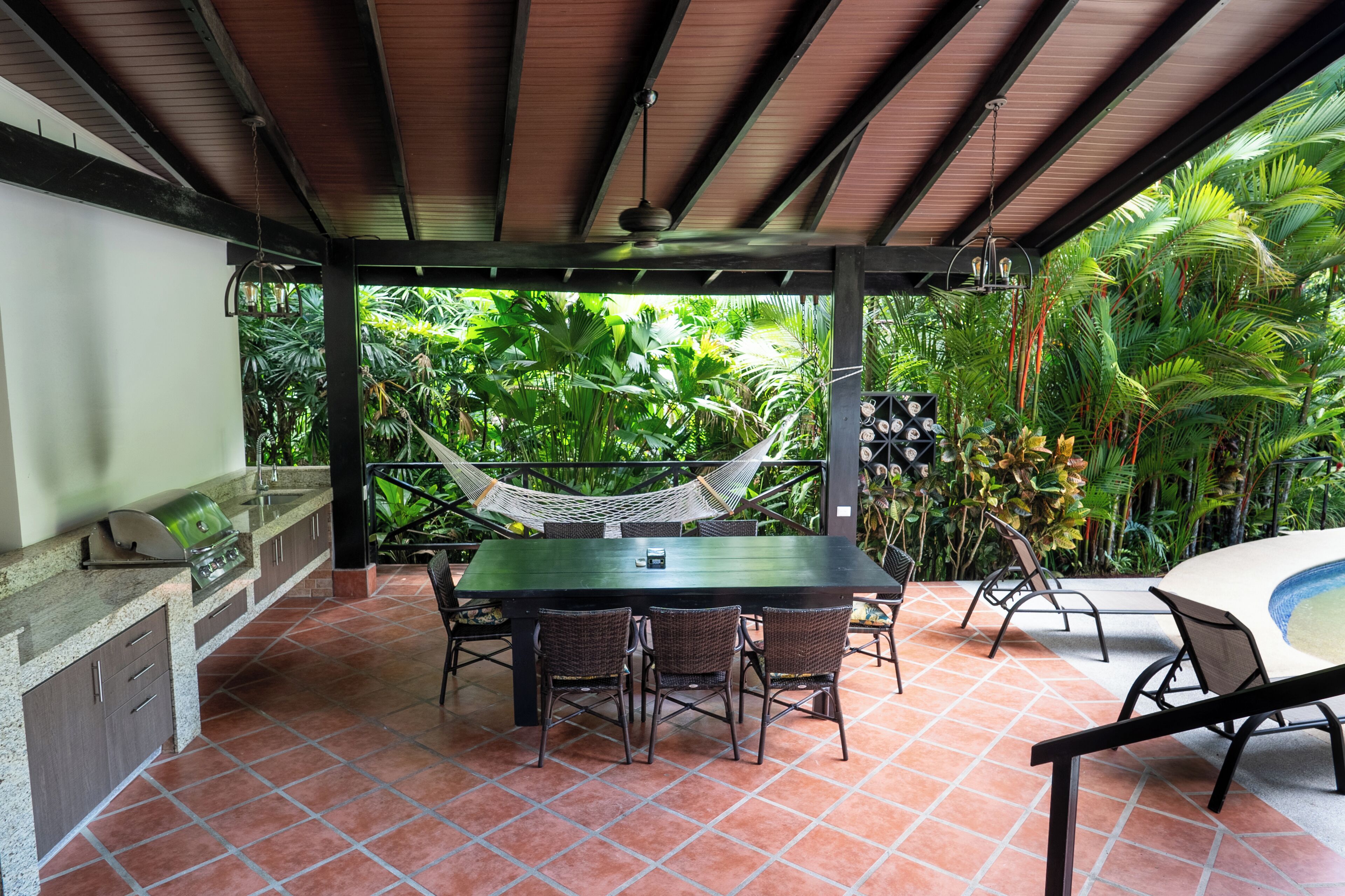An outdoor patio with a dining table, chairs, a grill, and a hammock.