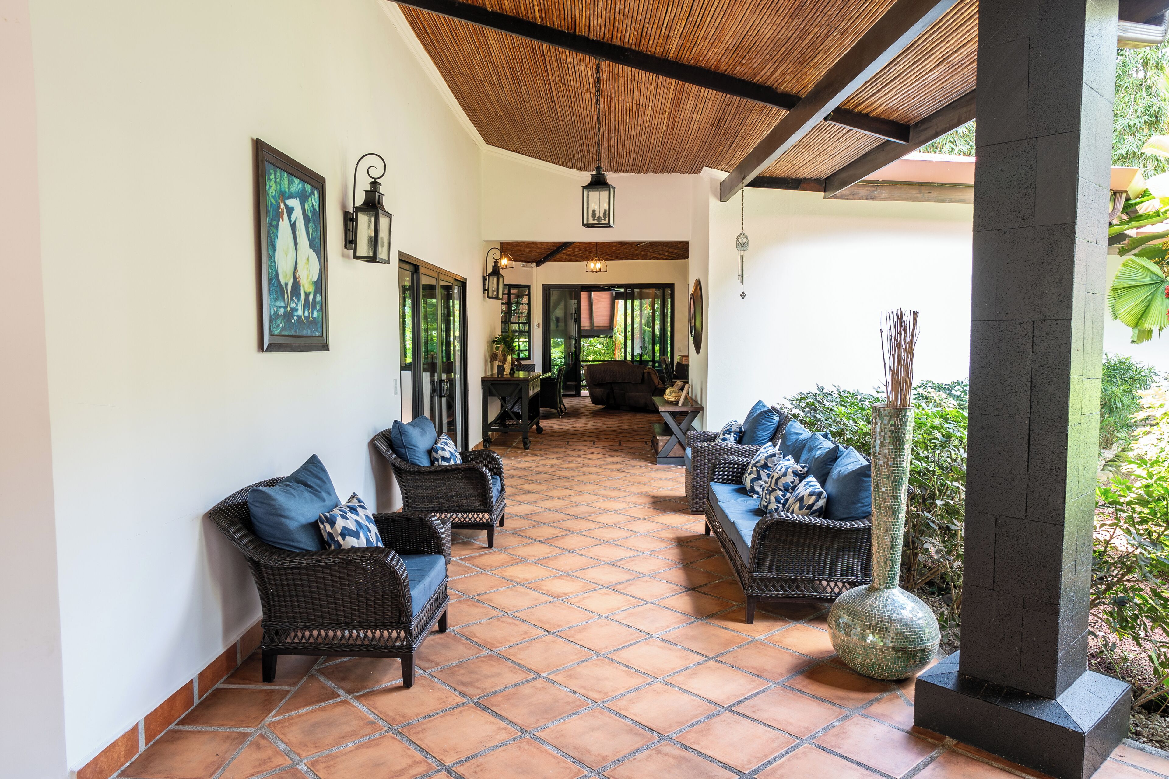 A covered outdoor seating area with wicker furniture and a tiled floor.