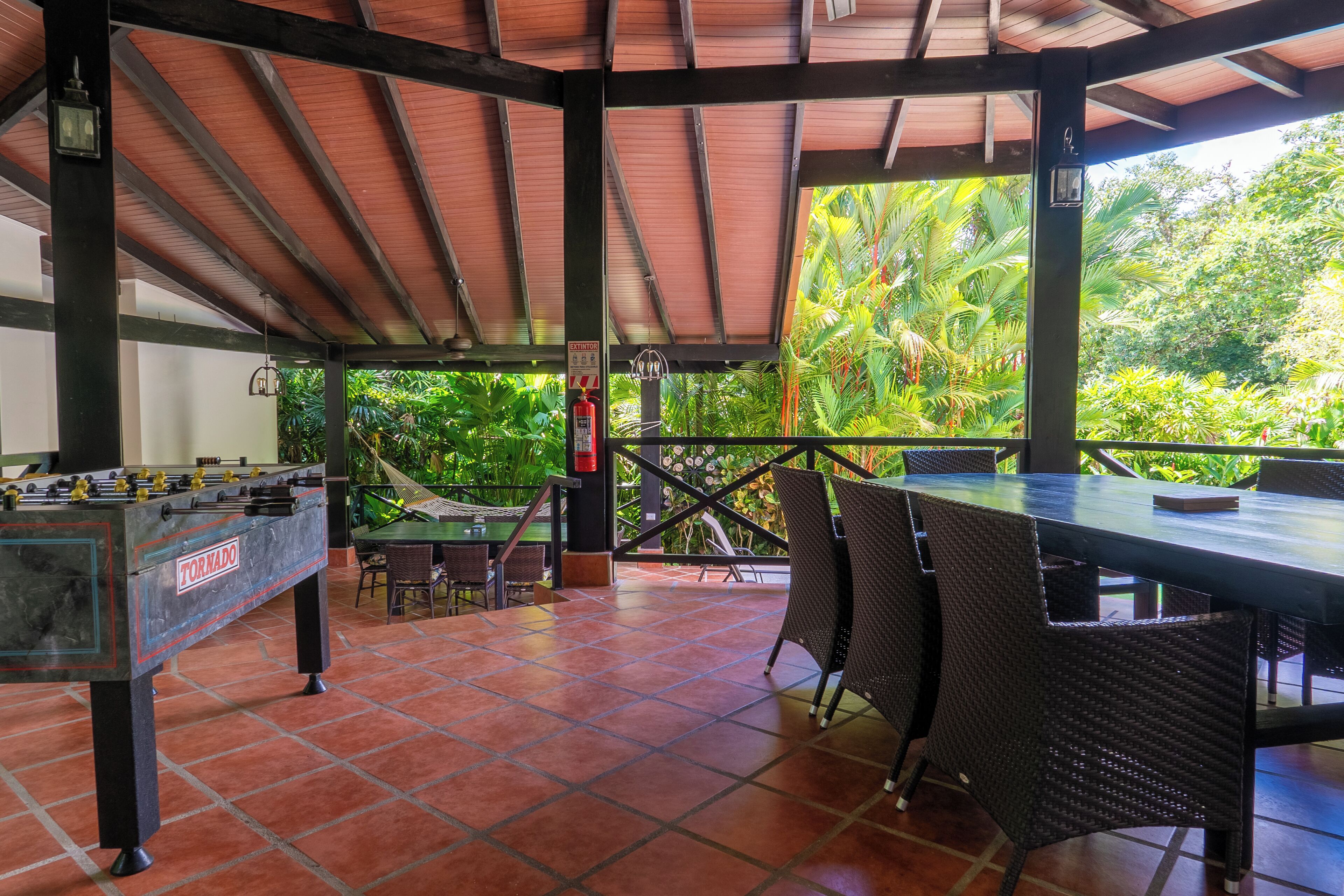 An outdoor covered patio with a foosball table, dining table, and chairs.