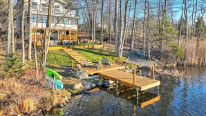 A lakeside property with a wooden dock, outdoor seating, and a house with a balcony. - Lakefront: Hot Tub + Fire Pit + Game Room + Pool (Tobyhanna)