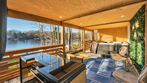 A wooden deck with a glass enclosure, a fireplace, and outdoor seating. - Lakefront: Hot Tub + Fire Pit + Game Room + Pool (Tobyhanna)