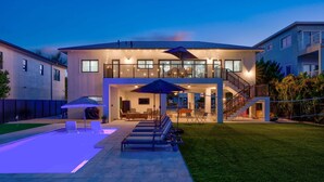 Una casa moderna de dos pisos con piscina, mobiliario exterior y una escalera que lleva a un balcón.