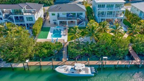 Una casa moderna de varios pisos con piscina, rodeada de exuberante vegetación y un muelle con un bote.