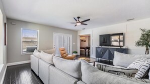 Un salon moderne avec un canapé d’angle, un téléviseur et un ventilateur de plafond.