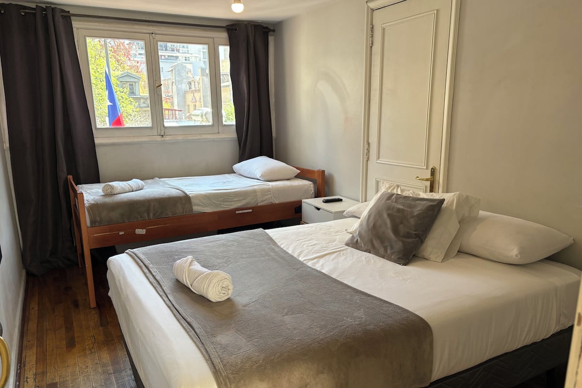Een hotelkamer met twee bedden, een raam met gordijnen, een nachtkastje en een deur.