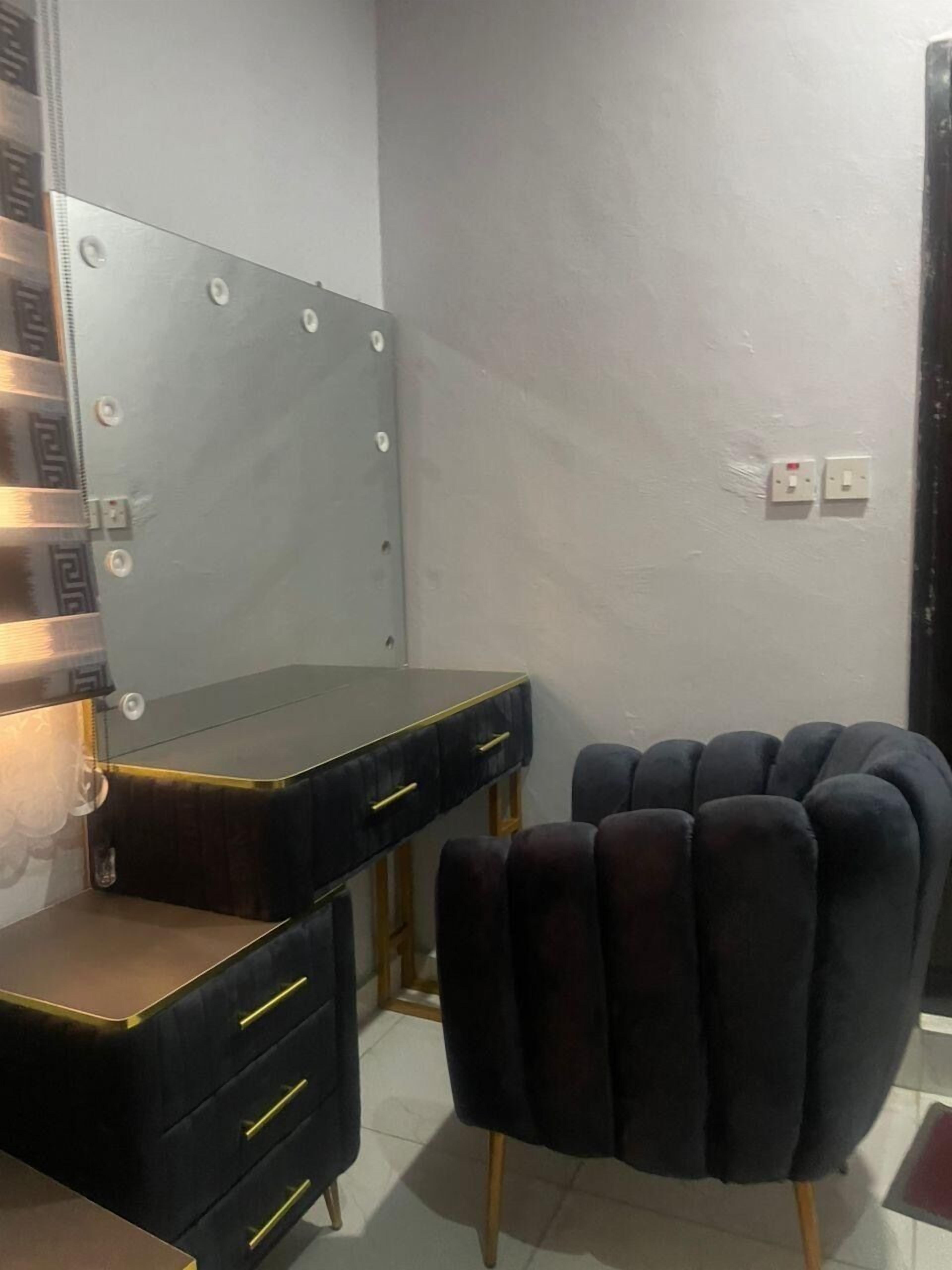 A room with a vanity mirror, a black desk with drawers, and a black upholstered chair.
