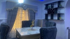 A dining area with a marble table, two upholstered chairs, a vase with flowers, and a decorative wall panel. - Muniz Global Apartments  (Lagos)