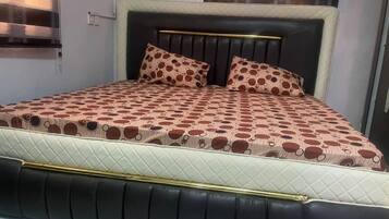 Een bed met een gewatteerd hoofdbord, twee kussens met een rond patroon, en een sprei met een vergelijkbaar ontwerp.