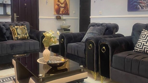 A modern living room with a black sofa set, a glass coffee table, and a decorative vase. - Muniz Global Apartments  (Lagos)