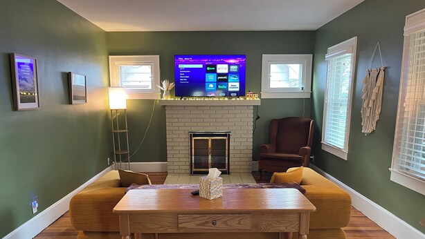 A living room with a fireplace, a TV mounted above it, and a comfortable seating area. - You'll love your stay at the Bohemian Bungalow centrally located in Terre Haute! (Terre Haute)