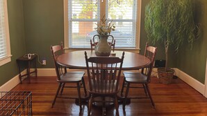 A dining area with a round table, wooden chairs, a chandelier, a vase with flowers, a potted plant, and a window with blinds. - You'll love your stay at the Bohemian Bungalow centrally located in Terre Haute! (Terre Haute)
