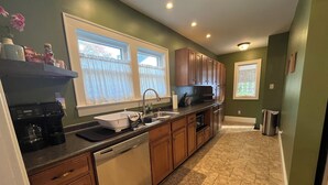 A kitchen with wooden cabinets, a dishwasher, a coffee maker, and a window with curtains. - You'll love your stay at the Bohemian Bungalow centrally located in Terre Haute! (Terre Haute)