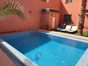 Une piscine avec un bord carrelé, une échelle et des chaises longues.