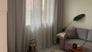 Un salon avec un canapé, une table sur laquelle est posée une bougie, une bouilloire et une grande plante.