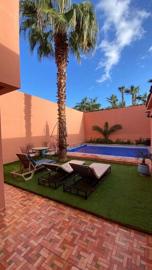 Ein Poolbereich mit Palme, Liegestühlen und einer gefliesten Terrasse.