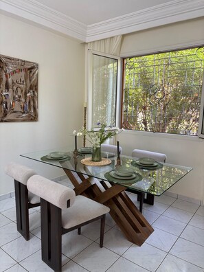 Un coin repas avec une table en verre, des chaises rembourrées et un tableau accroché au mur.